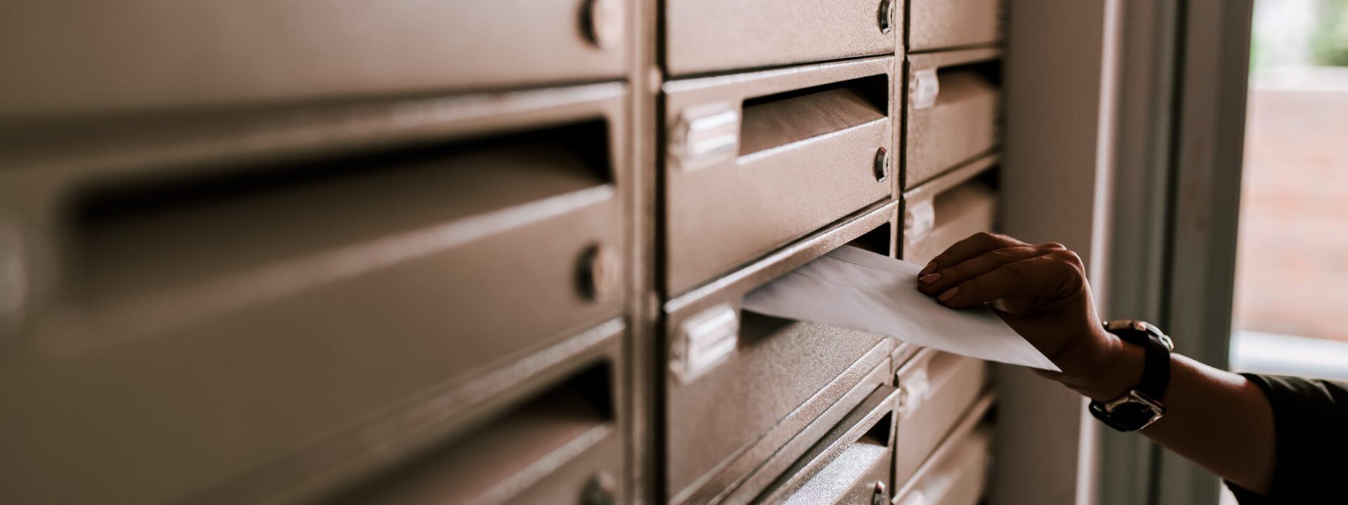 Female hand dropping envelope into mailbox in apartment building