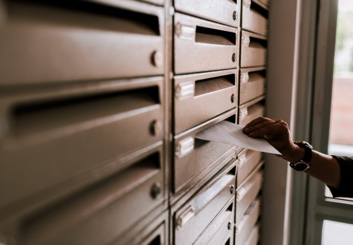 Female hand dropping envelope into mailbox in apartment building